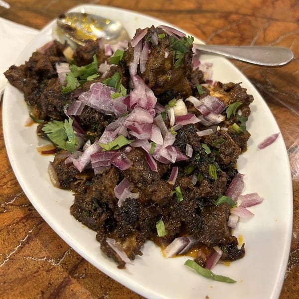 Chettinadu Indian Cuisine's dark, savory meat dish, garnished with red onions and fresh cilantro.