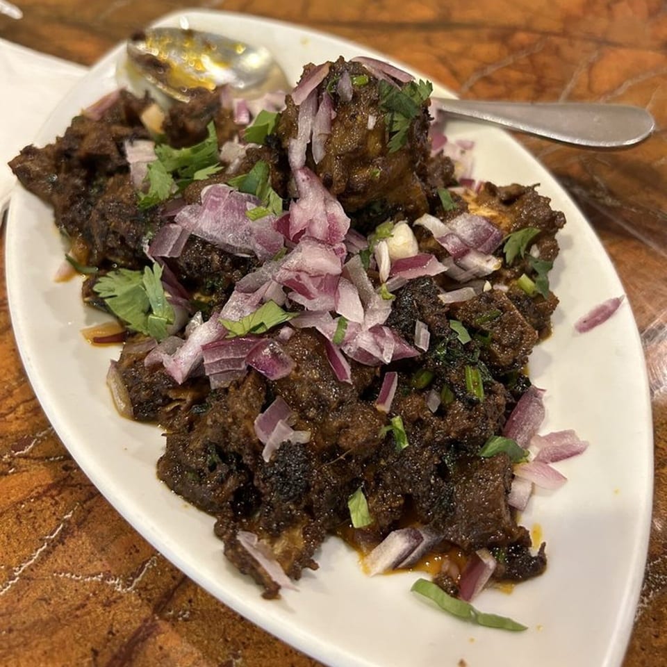 Chettinadu Indian Cuisine's dark, savory meat dish, garnished with red onions and fresh cilantro.