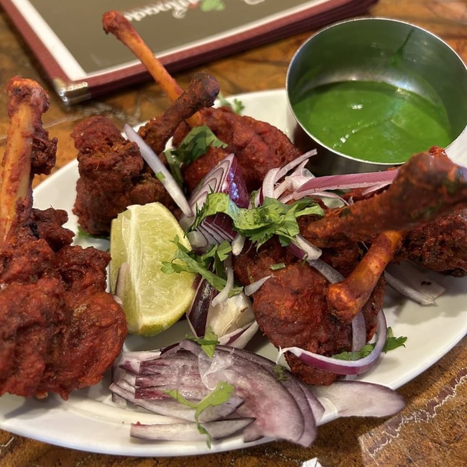 Chettinadu Indian Cuisine's Chicken Lollipops, garnished with lime, red onions, and cilantro, with green chutney.